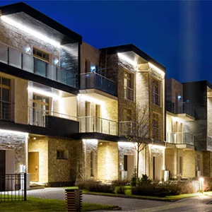 Stone-faced building at dusk with facade and soffit lighting across the balconies