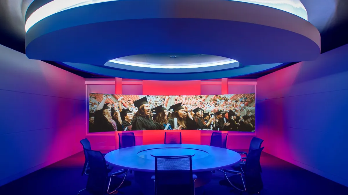 Circular briefing room with a cove-lit ceiling ring above a round table and a curved video wall
